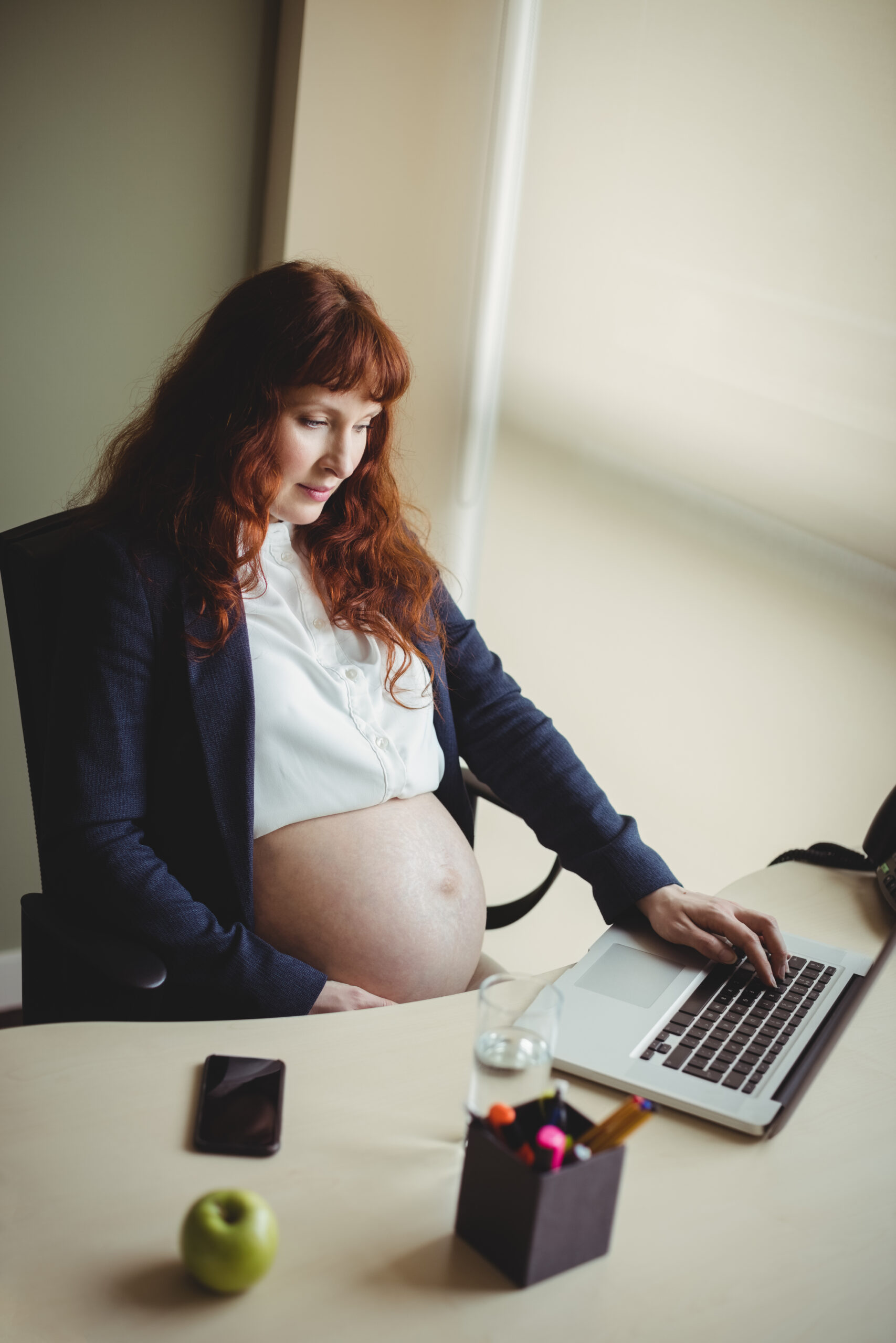 Pregnant businesswoman touching her belly while using laptop in office Pregnant businesswoman touching her belly while using laptop in office