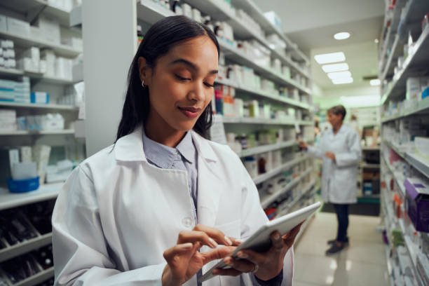 Smiling young female worker in pharmacy checking inventory using Stock Management Software